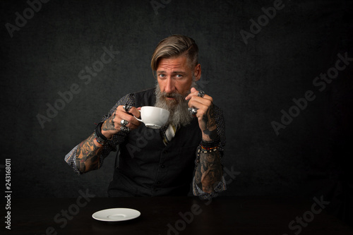 Porträt eines bärtigen Mannes mit einem Tasse Kaffee, vor dunklem Hintergrund	