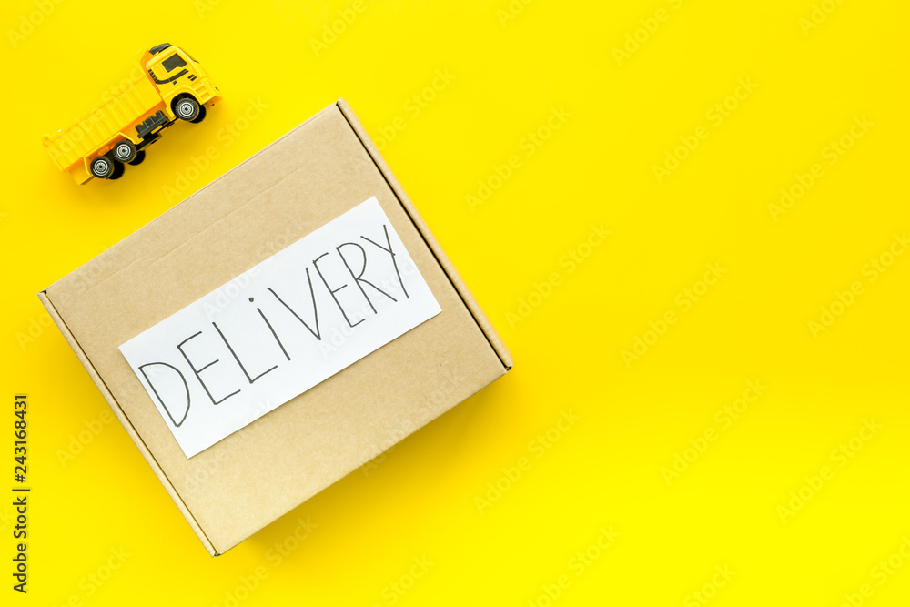 Cargo delivery concept. cardboard box with written word delivery near toy truck on yellow background top view copy space Cargo delivery concept. cardboard box with written word delivery near toy truck on yellow background top view copy space
