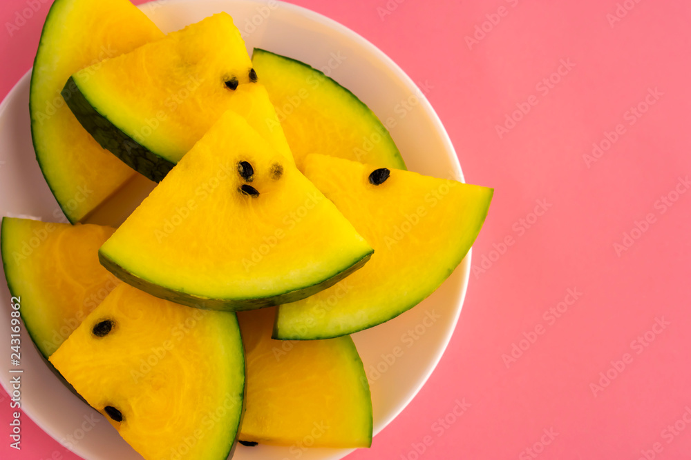 Ripe fresh slices of yellow watermelon in white plate on pink background. Top view. Copy space.