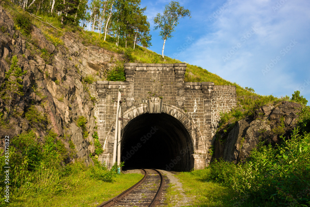 Stone arch tunnel in mountain on the Circum-Baikal railway. Summer landscape for travel in enigmatic Siberia. Transsiberian railway on coastline Baikal lake. Skillful work of mining engineers