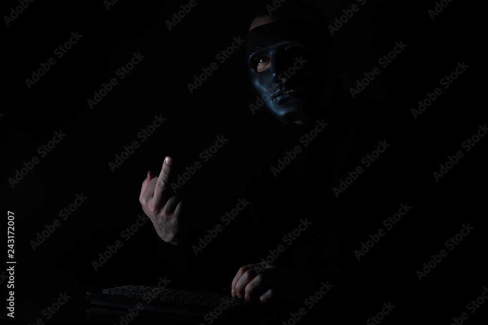 A man in a mask prints on the keyboard in the dark A man in a mask prints on the keyboard in the dark
