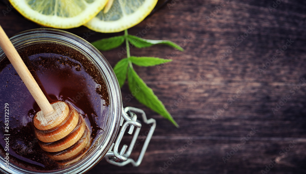 Honey and lemon. Honey stick and slices of sliced lemon on a wooden table. Tea in a cup and sweet lime honey in a jar. Honey and lemon. Honey stick and slices of sliced lemon on a wooden table. Tea in a cup and sweet lime honey in a jar.