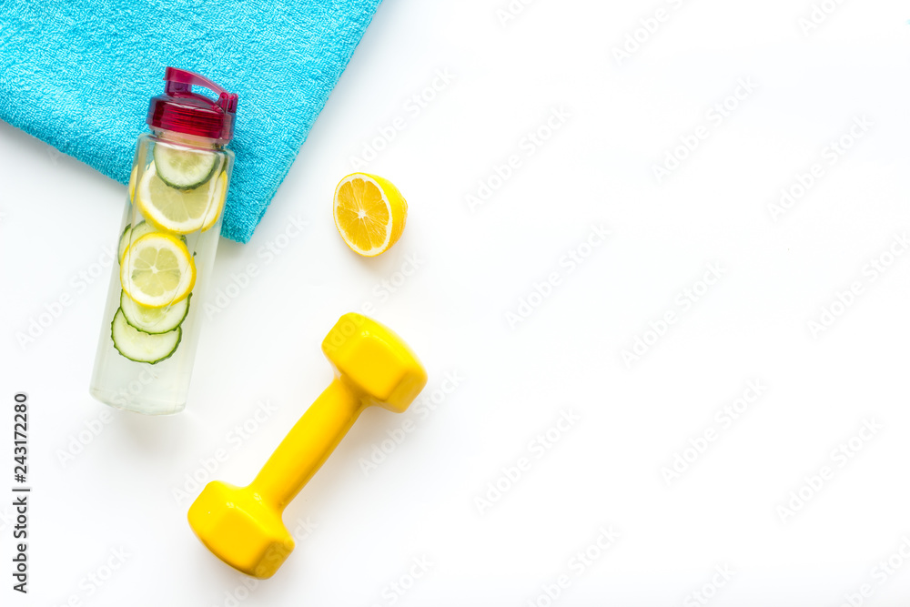 Healthy fruit water for sport, fitness. Bottle of water with lemon and cucumber near sport equipment dumbbells on white background top view copy space Healthy fruit water for sport, fitness. Bottle of water with lemon and cucumber near sport equipment dumbbells on white background top view copy space