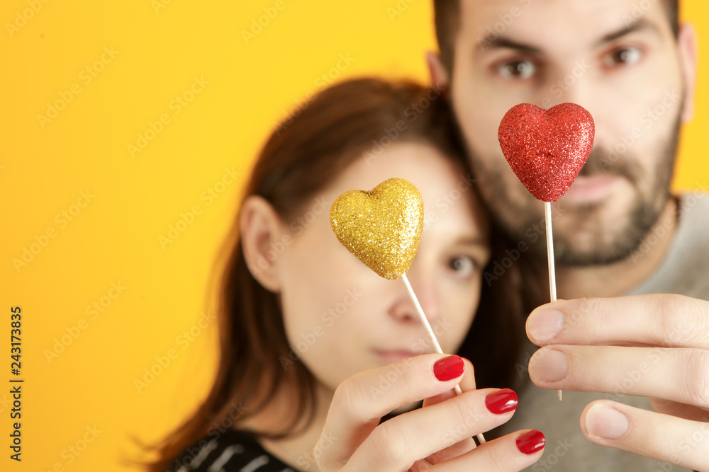 Young couple holding glitter hearts as a symbol of their love, studio shot on the bright yellow background Young couple holding glitter hearts as a symbol of their love, studio shot on the bright yellow background