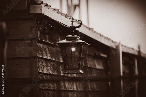 Old black outdoor lamp on wooden wall of old house in countryside. Holland, Netherlands . Image in sepia color style