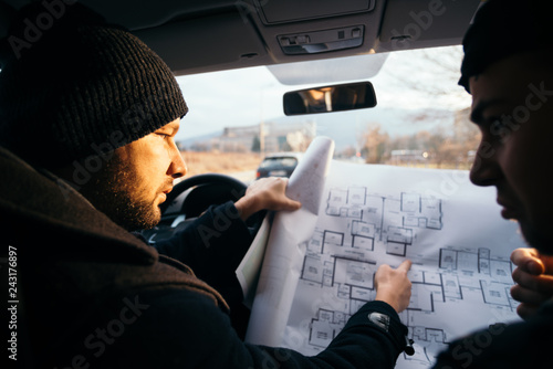 Cuadro en lienzo Two violent robbers sitting in a car looking at a blueprint of the building they want to rob while proudly showing off their guns
