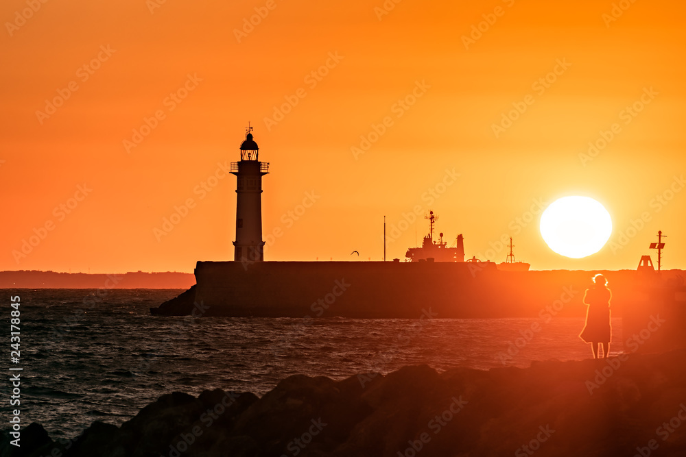 Coastal sunset scene with lighthouse; back light.