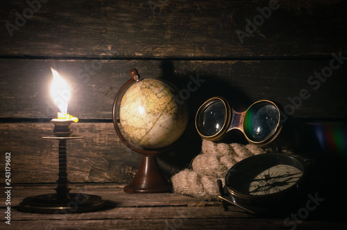 Travel or adventure background. Binoculars, globe, compass and mooring rope on the ship captain table in the light of burning candle.