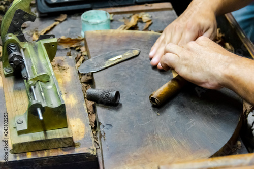 Traditional manufacture of cigars at the tobacco factory. Closeup of old hands making a cigar from tobacco leaves in a traditional cigar manufacture. Close up hands making a cigar from tobacco leaves