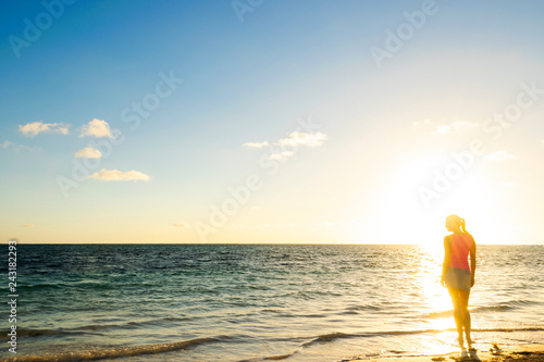 Girl silhouette looking beach sunset standing. Tropical beach. Travel concept. Girl looking at the sunset. Model girl silhouette over sunset sky. Swimming and splashing on summer beach over sunset.