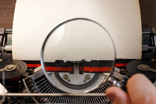 Vintage typewriter with blank paper and magnifying glass in a hand. Document investigation concept. Space for your text.  photo