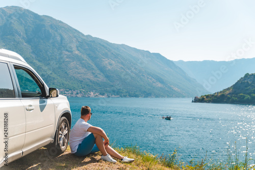 young man sitting near suv car at seaside with beautiful view of sea bay with mountains © phpetrunina14