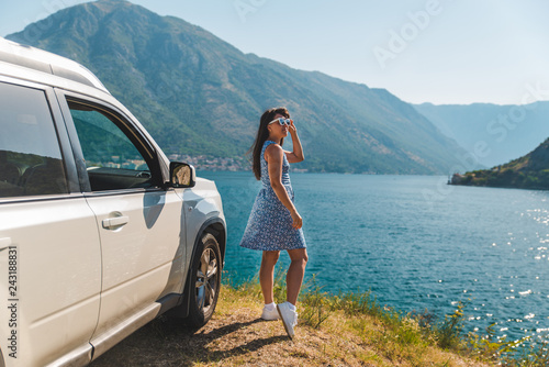 woman standing on cliff near white suv car with beautiful view of sea bay with mountains © phpetrunina14