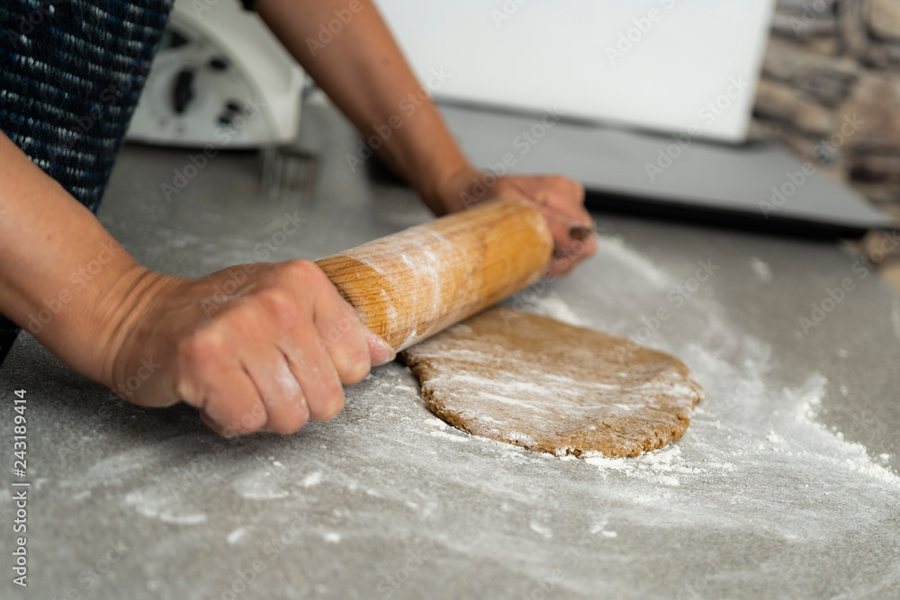 Two hands rolling, the biscuit dough evenly over flour with a rolling pin, making cookies and gingerbread in the kitchen Two hands rolling, the biscuit dough evenly over flour with a rolling pin, making cookies and gingerbread in the kitchen