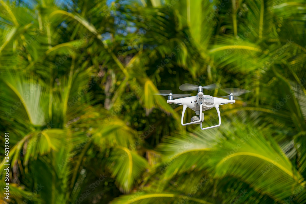 Drone in flight, green trees in the background, selective focus on the drone.