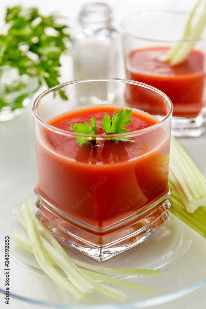 Fresh tomato juice. Tomato juice is poured into a transparent glass with parsley and herring, on a white background, illuminated by sunlight. Fresh tomato juice. Tomato juice is poured into a transparent glass with parsley and herring, on a white background, illuminated by sunlight.