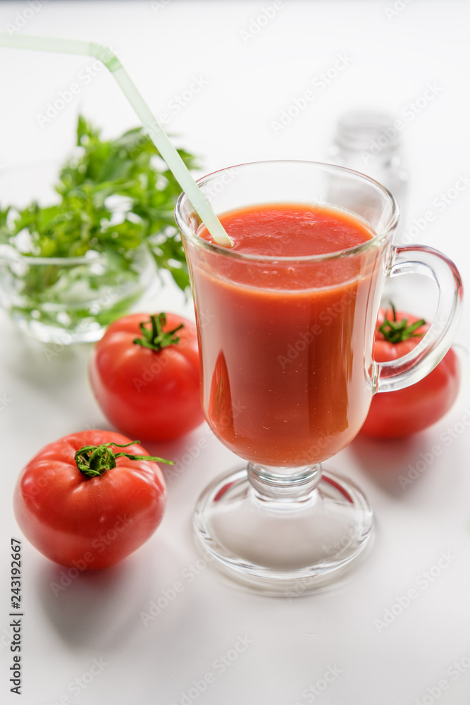 Tomato juice is poured into a transparent glass with parsley and herring, on a white background with cherry tomatoes, lit by sunlight. The most useful juice. Tomato juice from fresh tomatoes. Tomato juice is poured into a transparent glass with parsley and herring, on a white background with cherry tomatoes, lit by sunlight. The most useful juice. Tomato juice from fresh tomatoes.