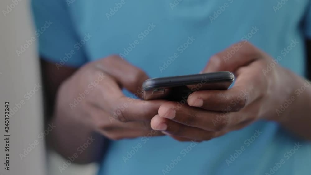 Close up shot of african american teenager wearing blue t-shirt texting on smartphone. Male hands using smartphone. Technology concept Close up shot of african american teenager wearing blue t-shirt texting on smartphone. Male hands using smartphone. Technology concept
