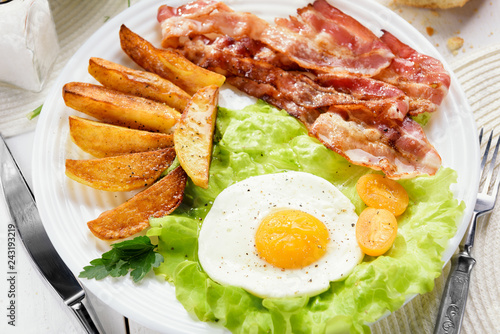 Morning breakfast with delicious fried bacon. French fries and tender egg, close-up.