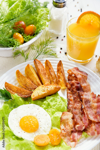 Fried bacon. French fries and egg with bacon on top in a white bowl, on a large table with greens.