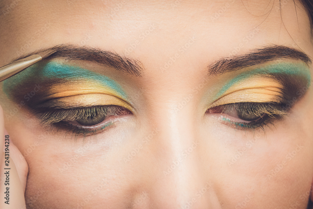Naklejka premium Professional makeup artist applying makeup for young woman in studio. Makeup detail.