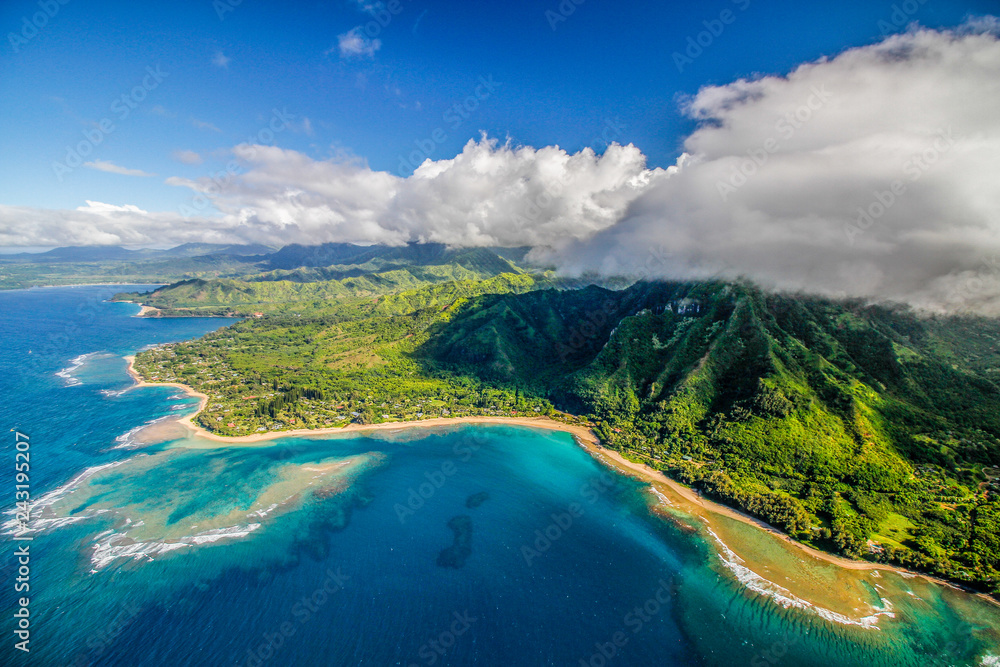 Aerial view of Na Pali Coast, Hawaii, taken from a helicopter with high white clouds over green cliffs and ocen bays with blue and crystal clear water, background