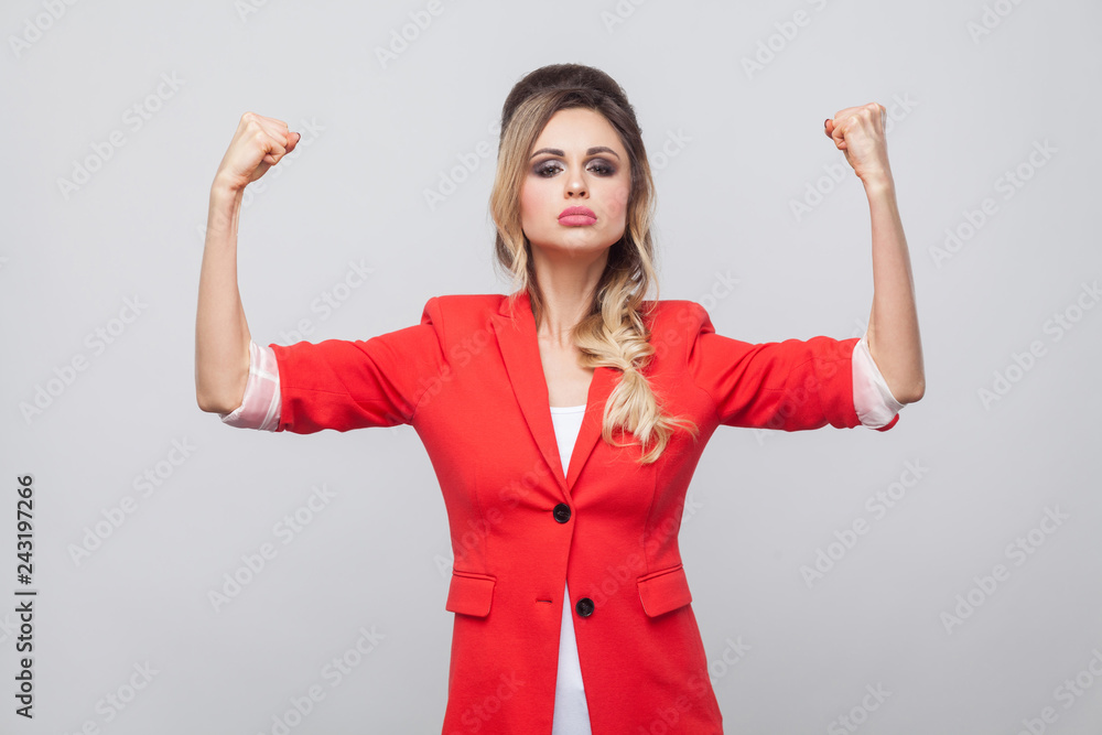 I am strong. Portrait of proud beautiful business lady with hairstyle and makeup in red fancy blazer, standing with raised arms and looking at camera. indoor studio shot, isolated on grey background. I am strong. Portrait of proud beautiful business lady with hairstyle and makeup in red fancy blazer, standing with raised arms and looking at camera. indoor studio shot, isolated on grey background.