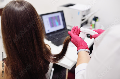 doctor dermatologist diagnoses the structure of the hair of a young pretty girl with a special tool - a trichoscope. Trichology, trichogram photo