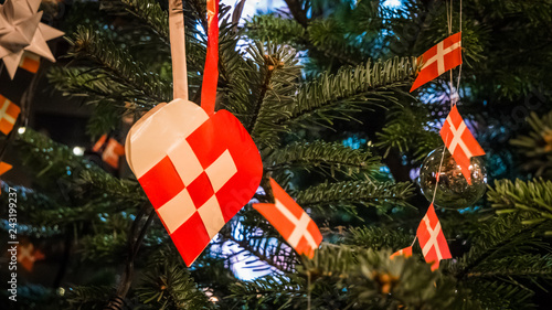 Traditional and typical Christmas Danish decoration made of paper woven heart or julehjerte with Danish flags on Christmas green pine tree