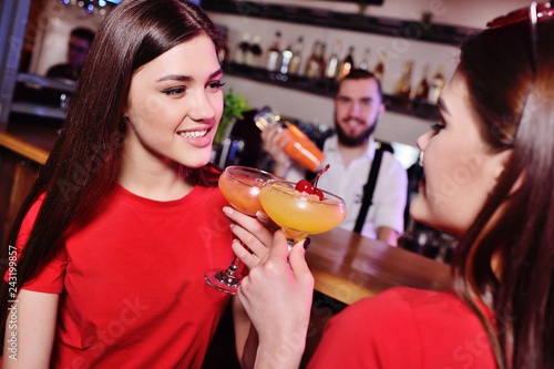 two young cute girls drink cocktails in a nightclub or bar  have fun  smile and talk to the bartender