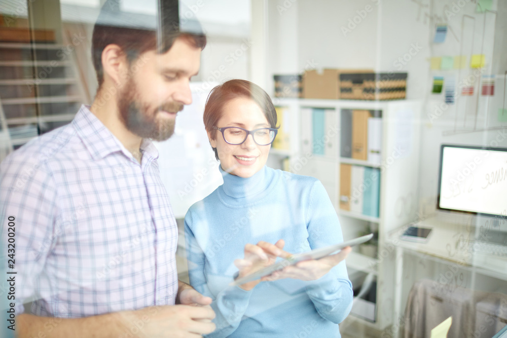 Young banker pointing at touchpad screen while making presentation of upgraded online data to colleague in office Young banker pointing at touchpad screen while making presentation of upgraded online data to colleague in office