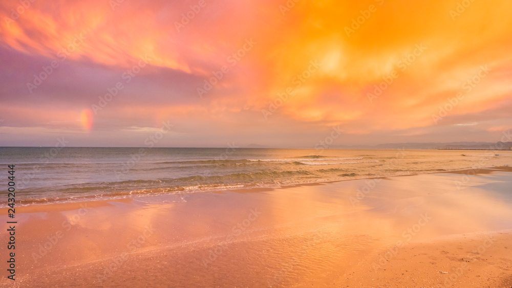 Rainbow and clouds are reflecting in the sea and puddle after the rain in Cullera, Valencia region, Spain.