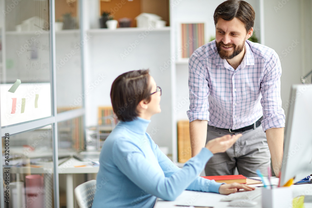 Two contemporary creative designers consulting about choice of graphics or organization moments in office Two contemporary creative designers consulting about choice of graphics or organization moments in office
