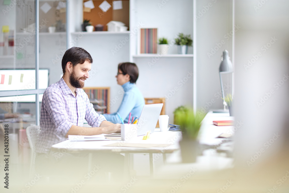 Young busy broker sitting by desk in front of laptop and entering data or looking for updates on stock market sites Young busy broker sitting by desk in front of laptop and entering data or looking for updates on stock market sites
