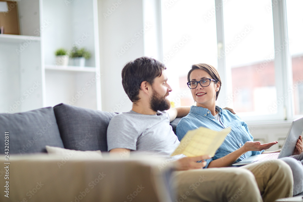 Affectionate couple relaxing on sofa and discussing online tours while looking for the best ones Affectionate couple relaxing on sofa and discussing online tours while looking for the best ones