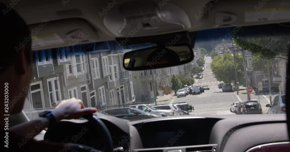 Man driving car down steep hill street during summer time - view from the back seat over the shoulder Man driving car down steep hill street during summer time - view from the back seat over the shoulder