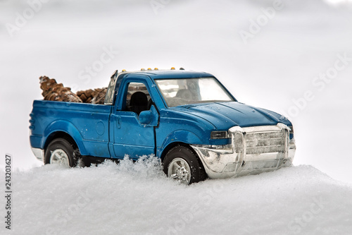 Blue toy pickup truck in snow. Stuck at snowdrift. Carrying fir cones in the back of a car body.