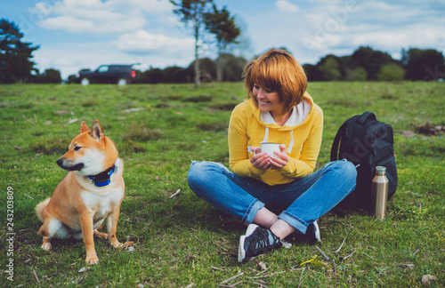 smile girl holding in hands cup drink, red japanese dog shiba inu on green grass in outdoors nature park, beautiful woman hipster and dogs friends, friendship lifestyle relax recreation meditation  © A_B_C