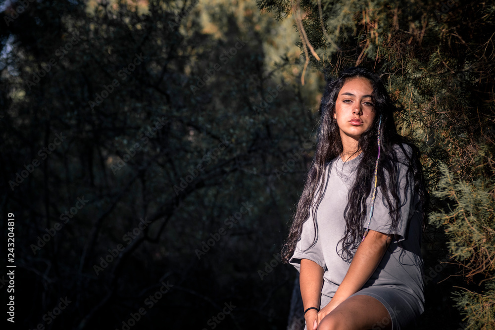Fototapeta premium Mujer joven morena sentada en el bosque a la derecha en la barandilla mirando a cámara