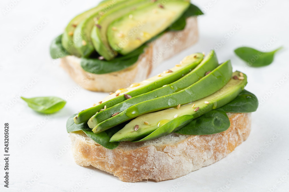 Two ciabatta toast with sliced avocado olive oil, spinach and flax and sesame seeds. Healthy vegetarian Breakfast on white background Two ciabatta toast with sliced avocado olive oil, spinach and flax and sesame seeds. Healthy vegetarian Breakfast on white background