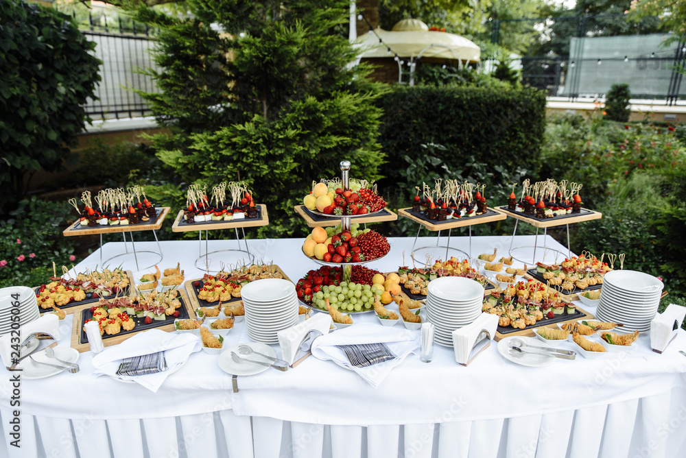 A buffet of various fruits and snacks in the open air. Strawberries, grapes, peaches, red currants outdoors