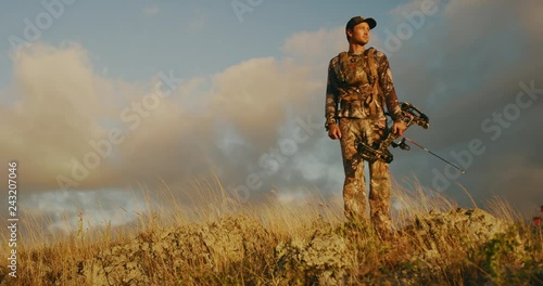 Orbit shot of bowhunter standing atop rocky knoll photo