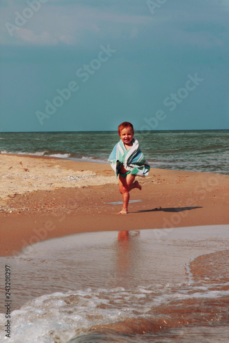 Cute little child girl wrapped in towel  running along thetropical beach after swimming in the sea.