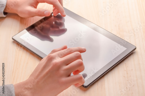 Black tablet in hands on a wooden table