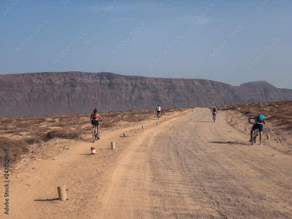 Persone in bicicletta su un percorso sterrato nell'isola della La Graciosa, Lanzarote, Isole Canarie. Spagna. Sullo sfondo El risco, la parte montuosa a Nord di Lanzarote Persone in bicicletta su un percorso sterrato nell'isola della La Graciosa, Lanzarote, Isole Canarie. Spagna. Sullo sfondo El risco, la parte montuosa a Nord di Lanzarote