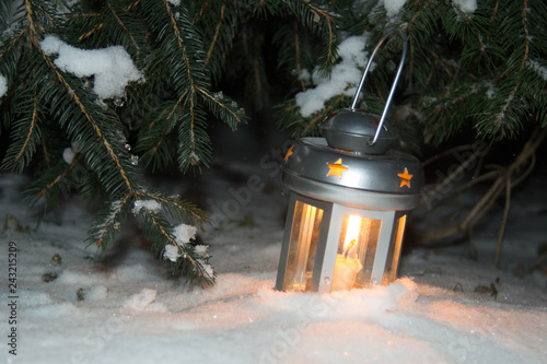 Lantern with burning candle on the snow in the evening. photo