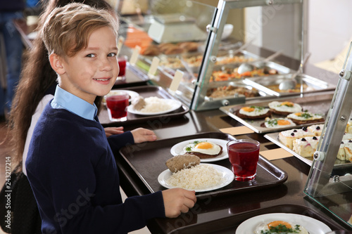 Cute boy near serving line with healthy food in school canteen photo