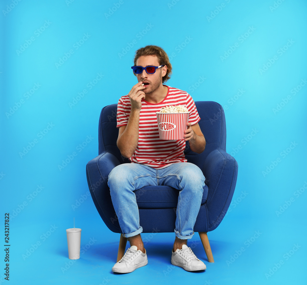 Naklejka premium Emotional man with 3D glasses, popcorn and beverage sitting in armchair during cinema show on color background