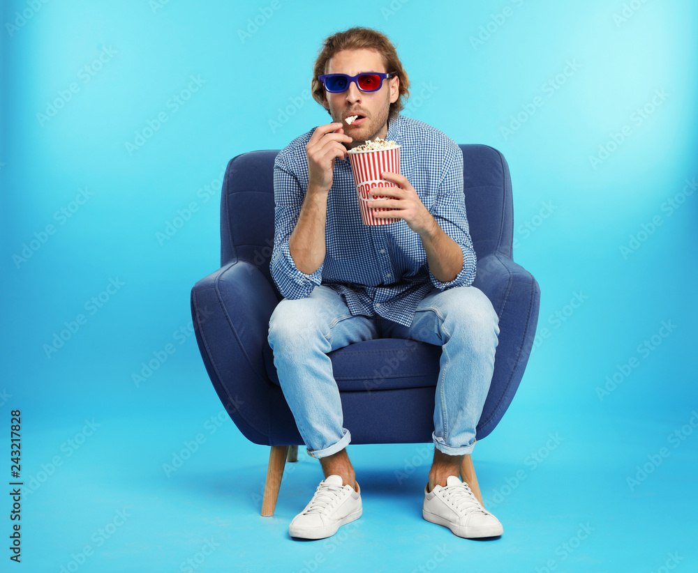 Naklejka premium Emotional man with 3D glasses and popcorn sitting in armchair during cinema show on color background