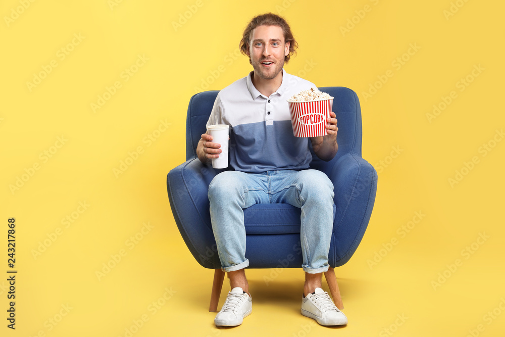 Emotional man with popcorn and beverage sitting in armchair during cinema show on color background Emotional man with popcorn and beverage sitting in armchair during cinema show on color background